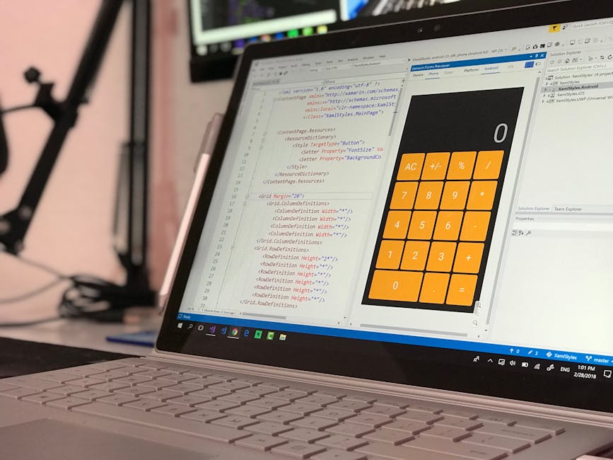 A person wearing a light blue shirt is seated at a desk during a home relocation or packing process, working on a laptop displaying a screen filled with colorful lines of code or data. The desk has se