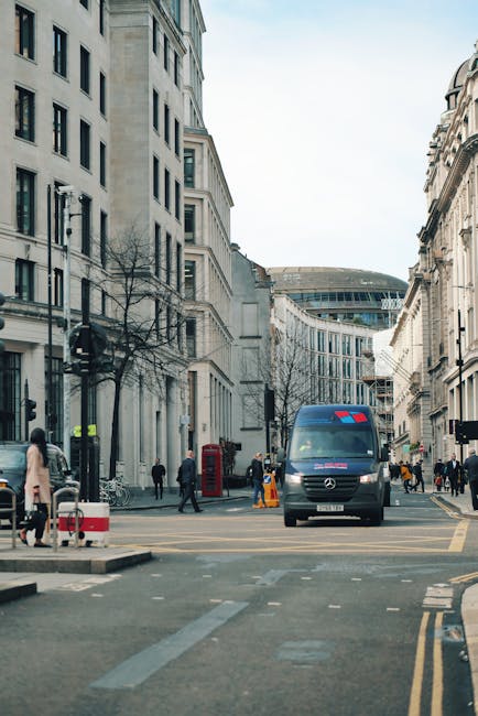 A narrow urban street scene showing two large multi-storey office buildings on either side, constructed with light-colored stone and concrete, featuring numerous rectangular windows. The street is pav